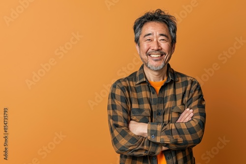 Portrait of a glad asian man in his 40s with arms crossed isolated in soft orange background photo