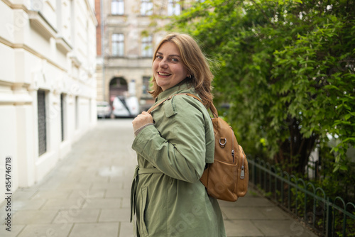 Portrait of a beautiful Caucasian female in a green coat, carrying a walking bag, smiling in a good mood in the city outdoors. High quality photo