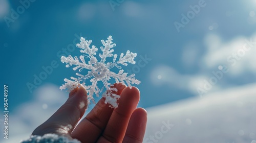A hand holding a delicate snowflake in a clear blue sky, with a sense of purity and uniqueness