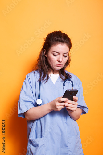 Canvastavla Portrait of nurse practitioner with stethoscope surfing the net on her mobile device