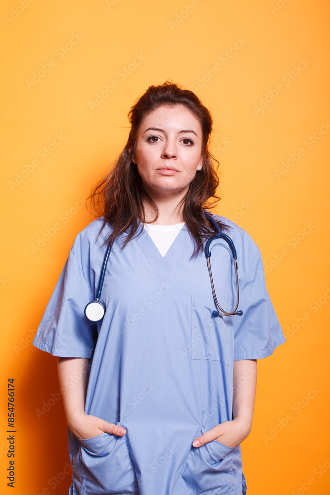 Nurse practitioner standing in front of isolated background with hands in her pockets. Portrait of female healthcare professional wearing scrubs and stethoscope posing for camera. Nurse practitioner standing in front of isolated background with hands in her pockets. Portrait of female healthcare professional wearing scrubs and stethoscope posing for camera.