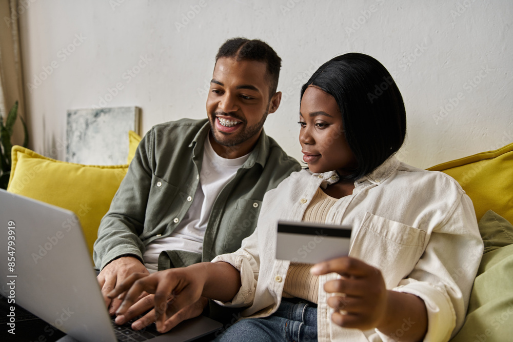 A loving African American couple shops online together at home, using a laptop and credit card. A loving African American couple shops online together at home, using a laptop and credit card.