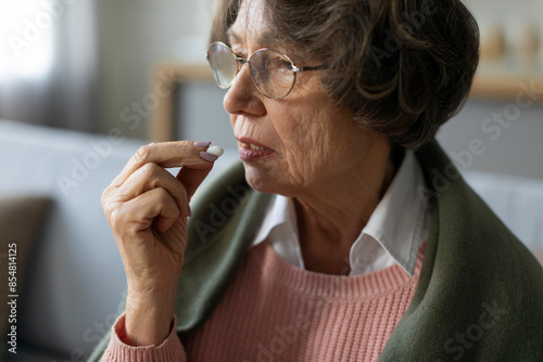 Treatment, medication at retirement. Elderly woman taking pill, senior lady holding hand with medicine near mouth photo