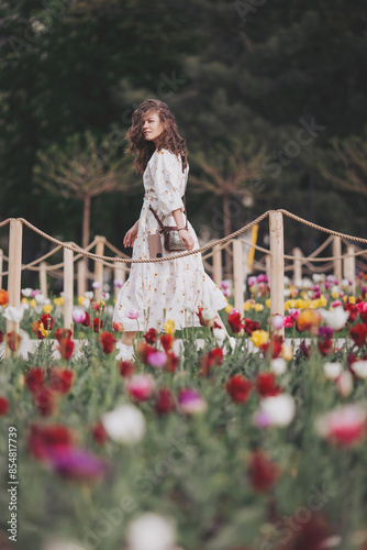 Young woman in a white dress is walking through the flower city garden. Happy woman in flower field. Sprins and summer. Romance and happiness. Young beautiful woman in tulip field photo