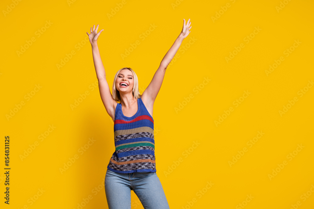 Photo of young blonde lady in striped casual singlet dancing raised arms up at summer party chilling out isolated on yellow color background Photo of young blonde lady in striped casual singlet dancing raised arms up at summer party chilling out isolated on yellow color background