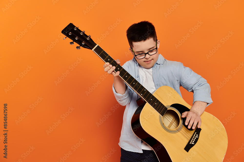 Obraz premium A young boy plays the guitar in front of an orange background.