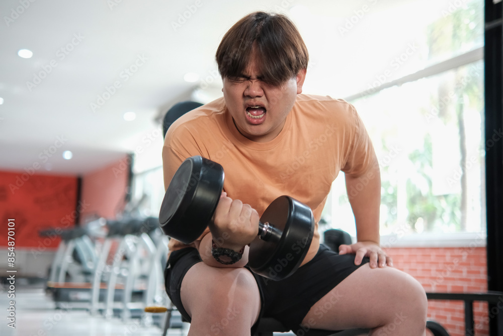 Overweight man grimacing while lifting dumbbell Overweight man grimacing while lifting dumbbell