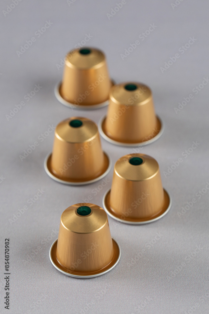 Five gold coffee capsules arranged on a neutral background, modern design. Advertising Five gold coffee capsules arranged on a neutral background, modern design. Advertising