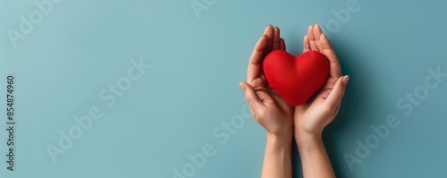 Two hands gently hold a red heart on a blue background