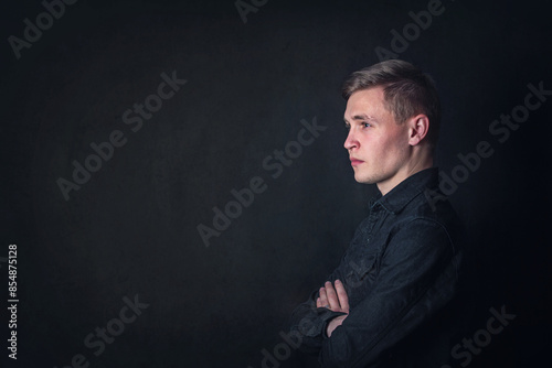 Serious contemplative young man side view portrait, looks pensive against a dark wall background. Male student reflects as have questions