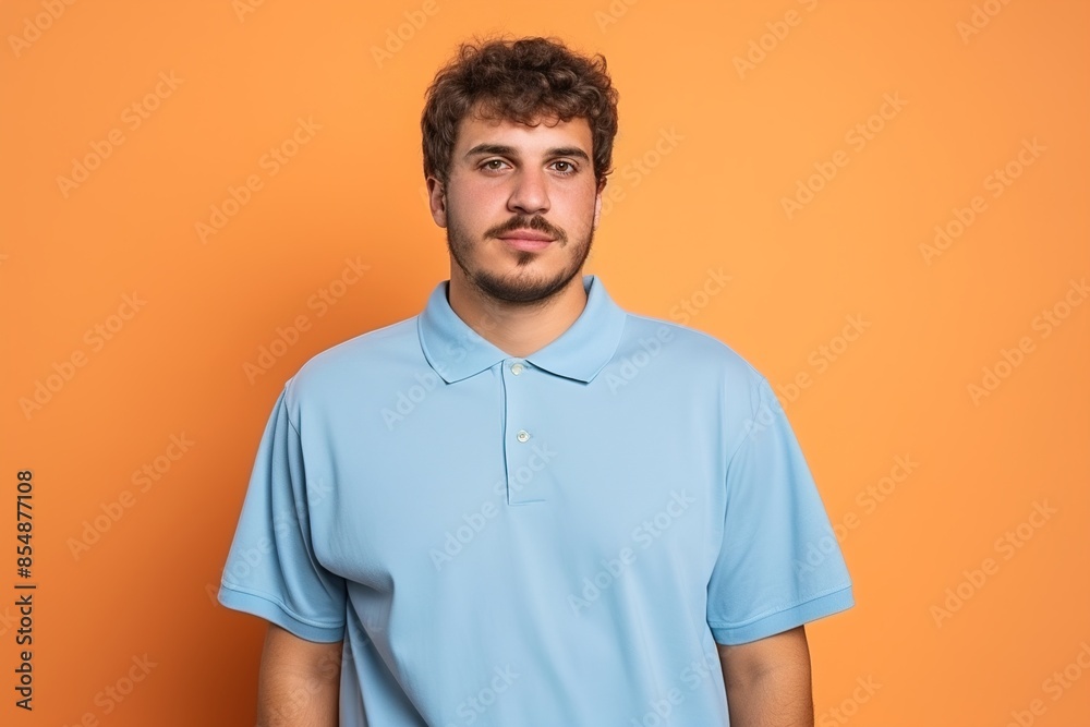 A man with a beard and a blue shirt is standing in front of an orange background A man with a beard and a blue shirt is standing in front of an orange background