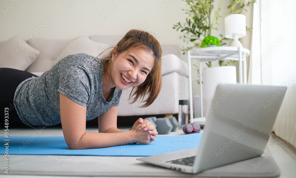 Pretty young woman doing yoga plank while watching online tutorial on laptop in living room. Pretty young woman doing yoga plank while watching online tutorial on laptop in living room.