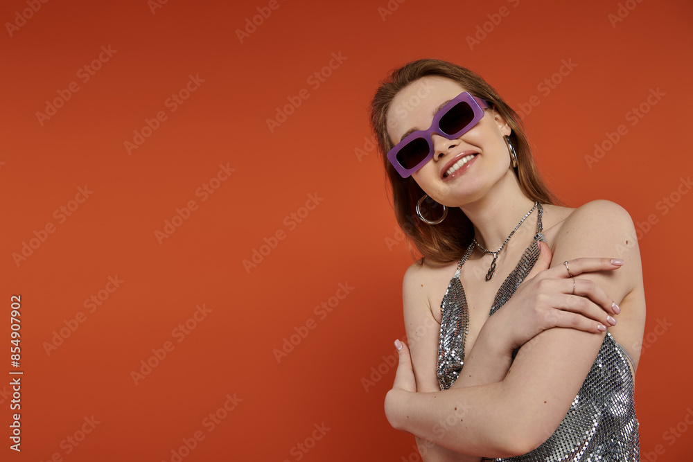 Fototapeta premium A young woman smiles playfully while posing against a vibrant orange backdrop.