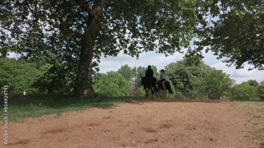 Two riders on horseback venture along a scenic trail in a lush London park, showcasing the tranquility of nature paired with recreational activities. Two riders on horseback venture along a scenic trail in a lush London park, showcasing the tranquility of nature paired with recreational activities.