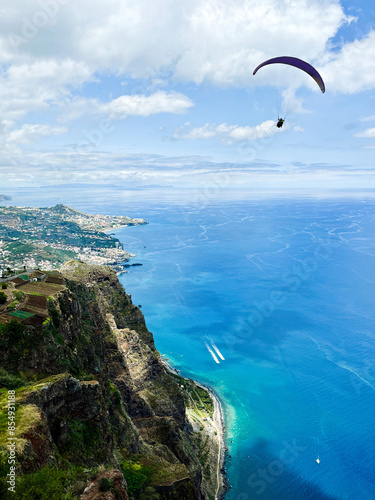 View from high ocean cliff to paraglider, green rock, city and ocean