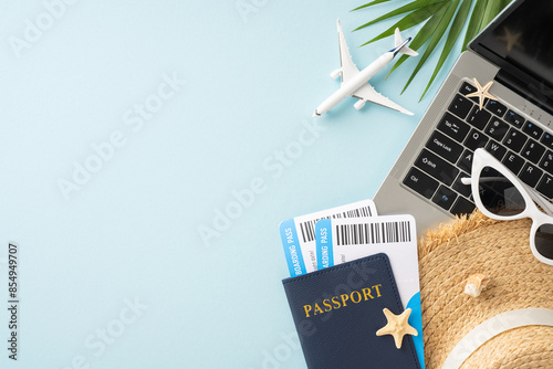 Overhead view of travel items including passport, boarding passes, laptop, sunglasses, and straw hat, suggesting summer vacation