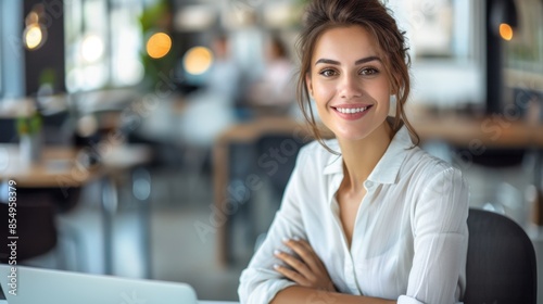 In a sleek office space, a young woman in a white shirt sits at her desk, beaming with confidence. The contemporary setting amplifies her professional demeanor and positive energy. 