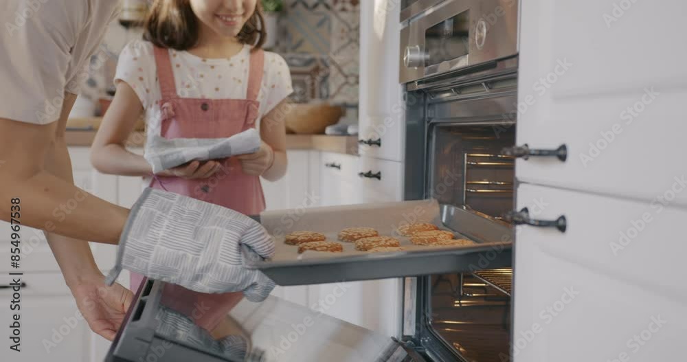 Mother and daughter taking hot ready biscuits out of oven preparing homemade cookies at home. Family lifestyle and meal preparation concept.