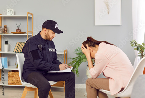 Police officer interviewing young woman robbery victim covering face with hands after breaking into home. Policeman writing down testimonies to investigate crime scene of house burglary. photo