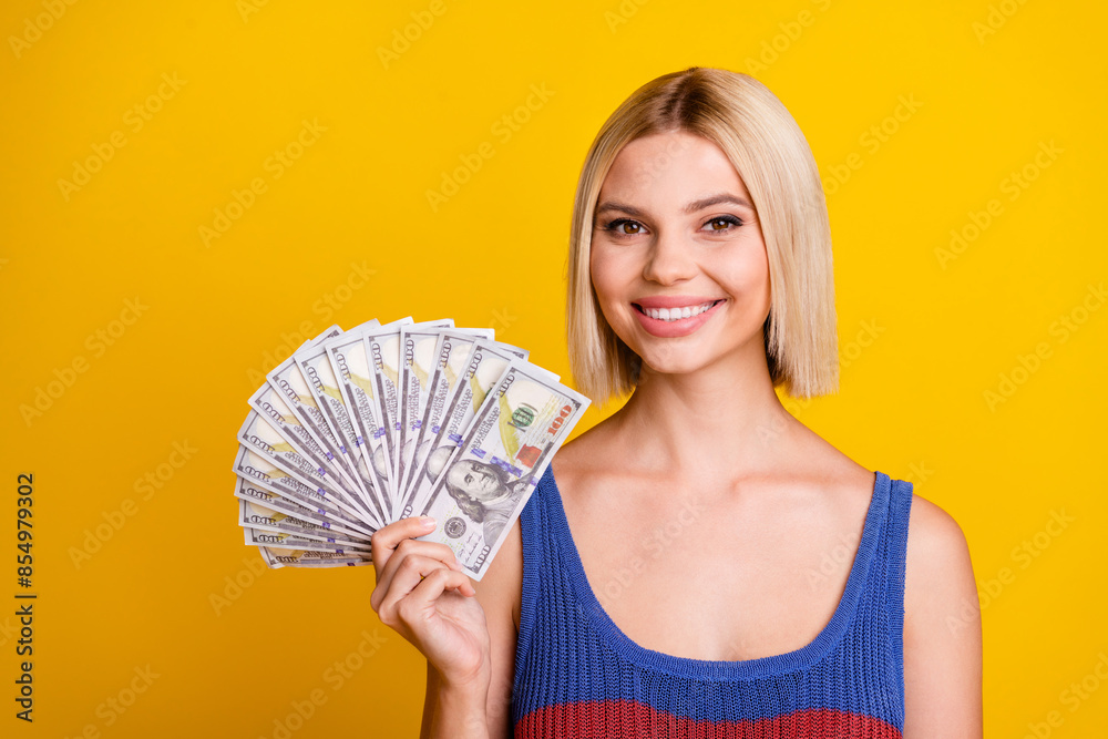 Portrait photo of young blond business lady in singlet holding her weekly salary for shopping isolated on yellow color background Portrait photo of young blond business lady in singlet holding her weekly salary for shopping isolated on yellow color background