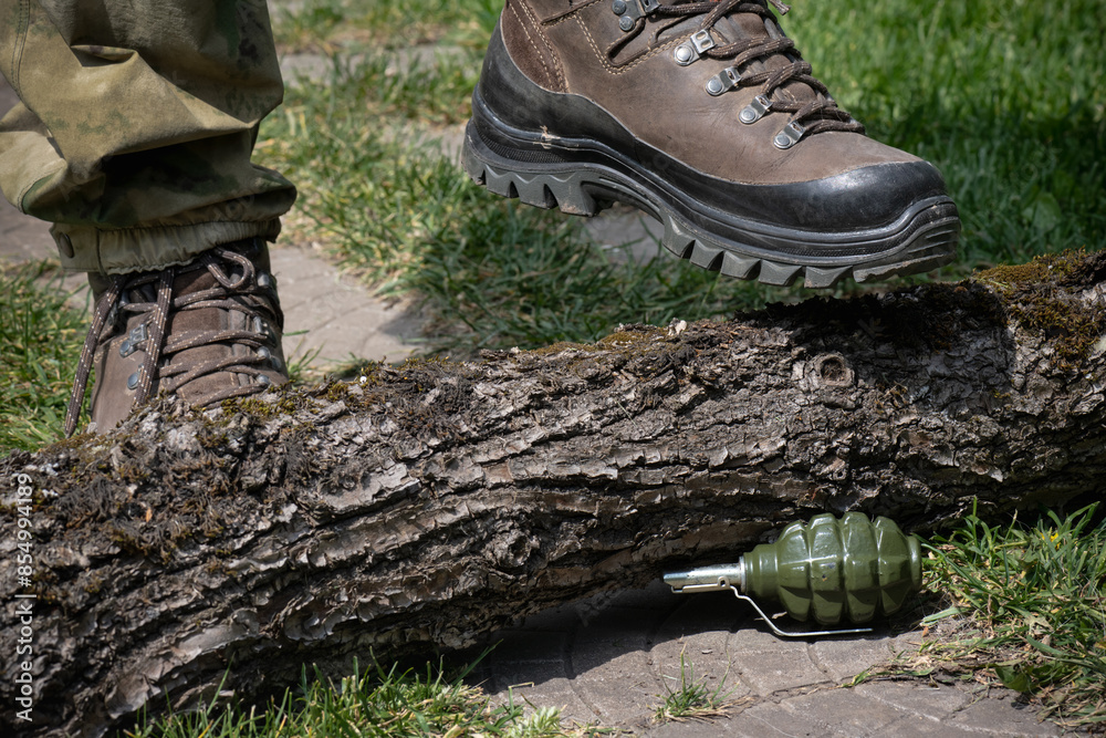 Man`s foot in military boot steps over the log to Booby Trap Landmine made from hand grenade installed on the ground on the path risks exploding Man`s foot in military boot steps over the log to Booby Trap Landmine made from hand grenade installed on the ground on the path risks exploding