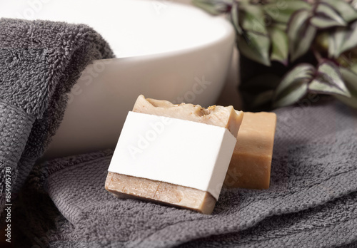 Soap bar with blank label near grey towels, plant and basin on wood in bathroom, mockup photo