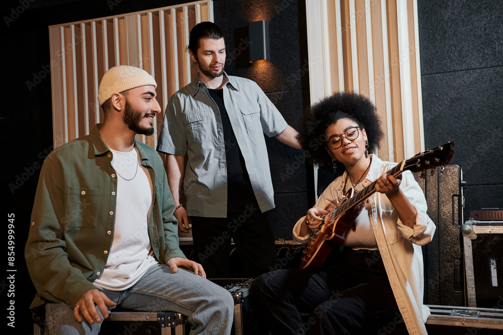 Obraz premium Three individuals sitting in a recording studio, immersed in playing a guitar and creating music together.