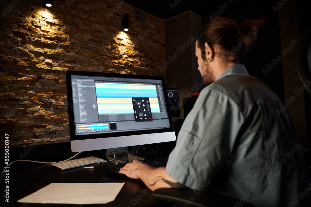 A man engrossed in working on a computer, creating music in a professional recording studio during a band rehearsal. A man engrossed in working on a computer, creating music in a professional recording studio during a band rehearsal.