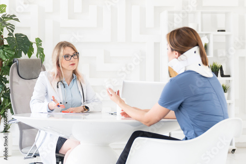 Female doctor traumatologist-orthopedist explaining to her patient with serious neck injury in neck brace about importance of cervical collar for healthy cure