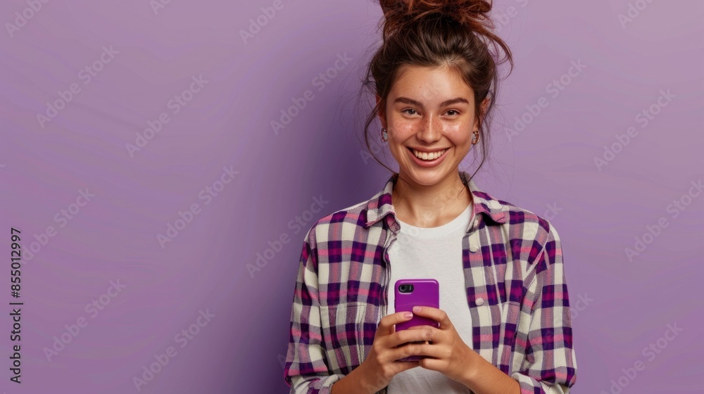 Happy pretty gen z blonde young woman model holding smartphone looking at cell texting message, smiling girl using mobile apps on cell phone standing isolated on purple background with cellphone. Happy pretty gen z blonde young woman model holding smartphone looking at cell texting message, smiling girl using mobile apps on cell phone standing isolated on purple background with cellphone.