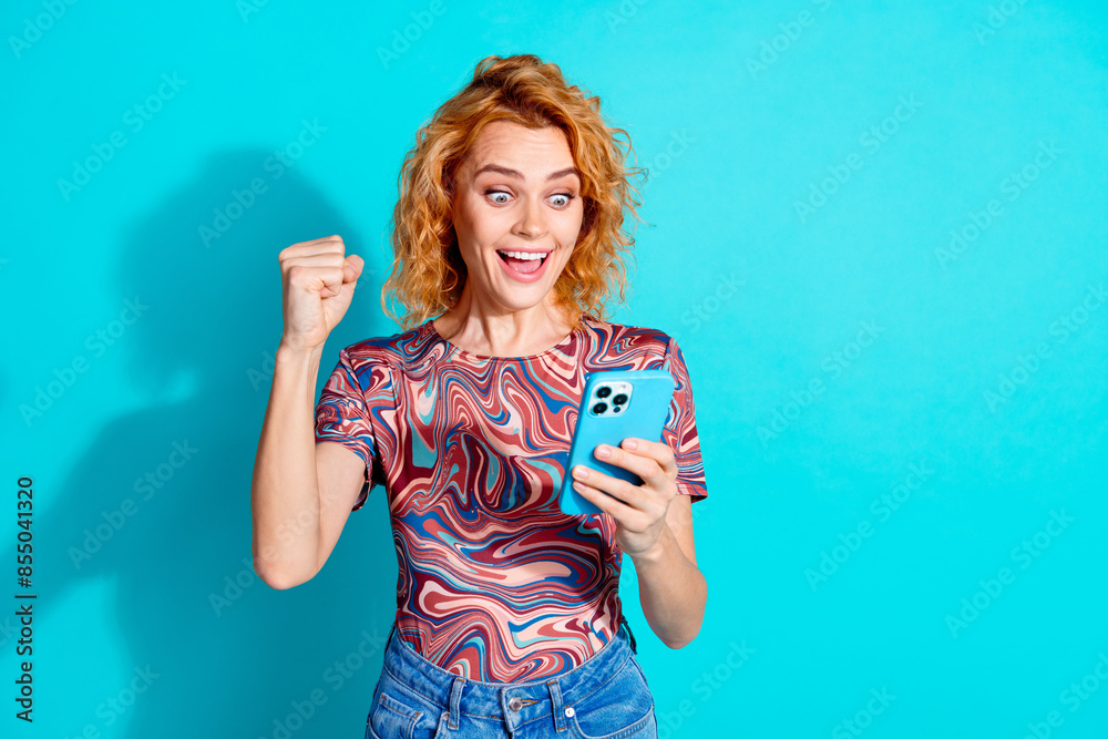 Portrait of nice lady use smart phone raise fist wear t-shirt isolated on teal color background Portrait of nice lady use smart phone raise fist wear t-shirt isolated on teal color background