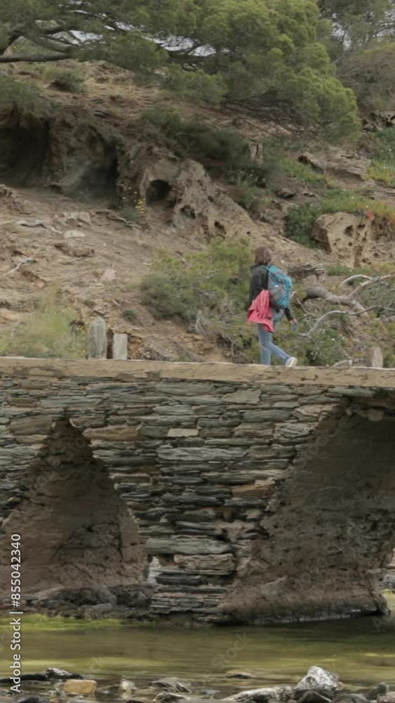 Cadaques, Province Of Girona, Catalonia, Spain. Young Woman Tourist Walking On Stone Bridge To Mirador. Cadaques, Province Of Girona, Catalonia, Spain. Young Woman Tourist Walking On Stone Bridge To Mirador.