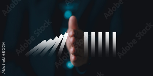 Photos Business's hand holding a glowing domino, protect business from the economic crisis