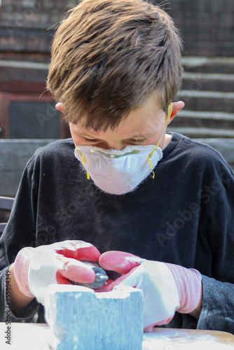 фотографія Boy wearing protective mask and gloves carving a stone block outdoors