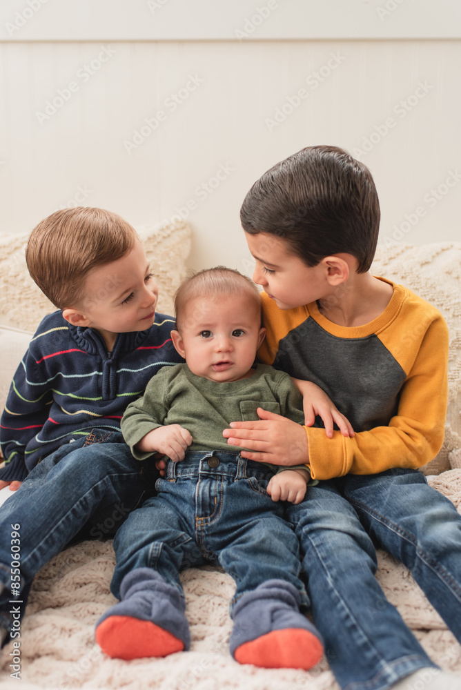 Toddler brothers comforting crying baby brother while sitting on bed Toddler brothers comforting crying baby brother while sitting on bed