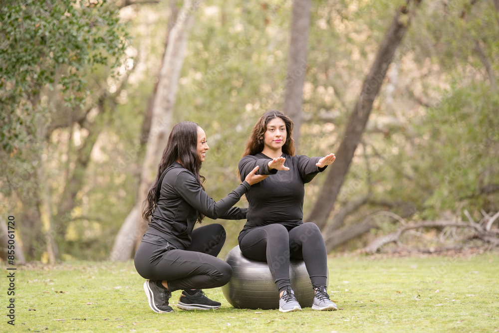 Women trainer showing a person on a workout ball in the woods Women trainer showing a person on a workout ball in the woods