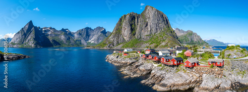 A picturesque view of red cabins perched on the rocky shore of a fjord in Norway, with towering mountains in the background. Hamnoy fishing village on Lofoten Islands, Norway with red rorbu houses photo