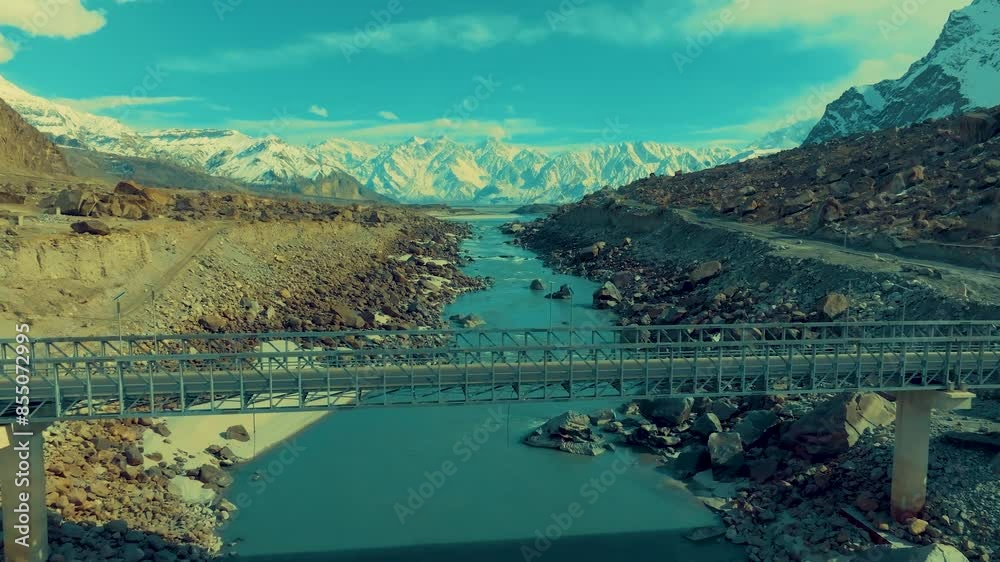 Aerial view capturing a bridge spanning a blue river amidst rugged, rocky terrain. The image illustrates infrastructure blending with natural beauty. Pull Back, Rising Shot Aerial view capturing a bridge spanning a blue river amidst rugged, rocky terrain. The image illustrates infrastructure blending with natural beauty. Pull Back, Rising Shot