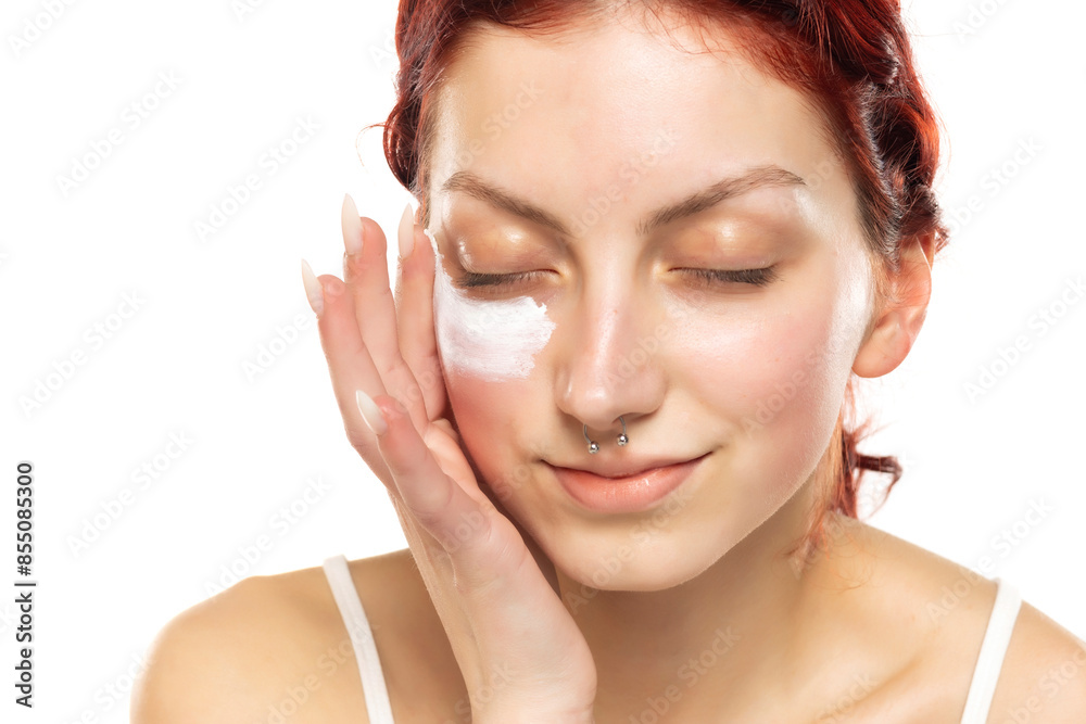 Young red haired woman applying face skin cosmetics on a white background Young red haired woman applying face skin cosmetics on a white background