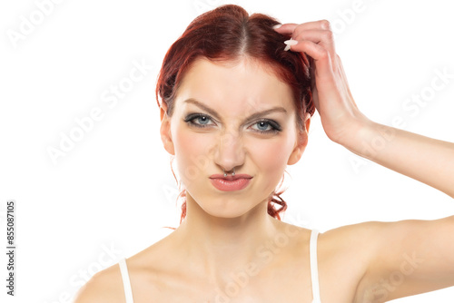 Portrait of a young uncertain frowning  woman with makeup and nose piercing on a white background