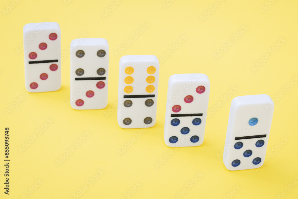 Five white dominoes with colored dots lie on a yellow background. Five white dominoes with colored dots lie on a yellow background.