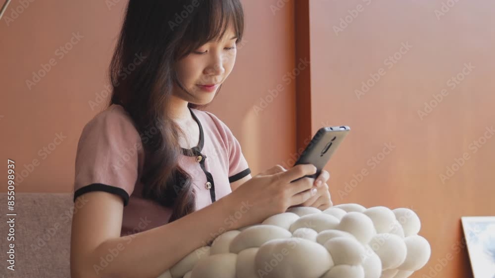 A young Asian woman is drinking from a black cup with a straw while looking at her phone A young Asian woman is drinking from a black cup with a straw while looking at her phone