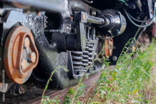 A close-up of the detailed mechanics of a freight train's suspension system, focusing on the metal springs, bolts, and hydraulic components. 