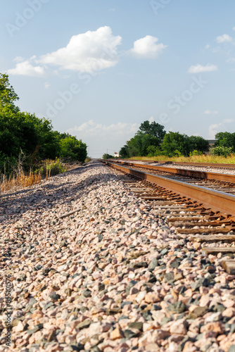 A low-angle view of railway tracks stretching into the distance on a clear, sunny day.