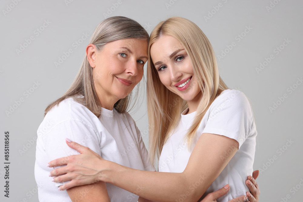 Family portrait of young woman and her mother on light grey background