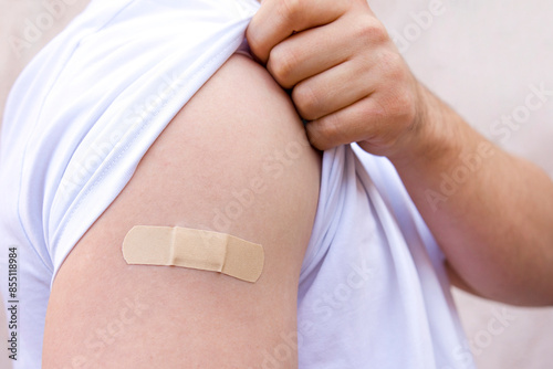 Plaster on a man's shoulder. The man pulls up the sleeve of his T-shirt.
