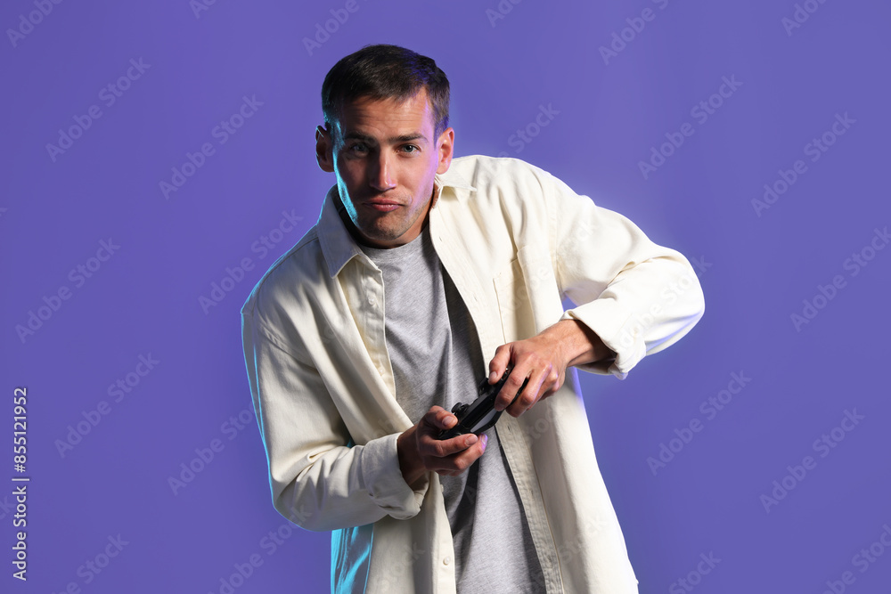 Fototapeta premium Man playing video games with controller on violet background
