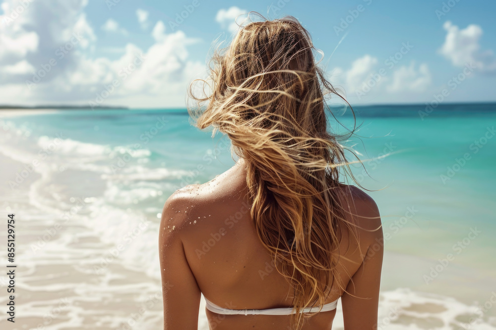 Naklejka premium Young beautiful woman with long windy hair walking on the beach in bikini, back view 