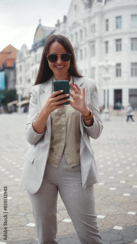 Vertical shot of a smiling businesswoman standing in the center of an urban city smiling while typing a message on her phone Vertical shot of a smiling businesswoman standing in the center of an urban city smiling while typing a message on her phone