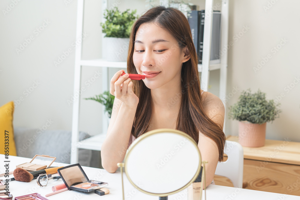 Skin care, beauty cosmetics concept, pretty asian young woman, girl make up face by applying red lipstick, lips balm on her mouth, looking at the mirror at home. Female look with natural fashion style Skin care, beauty cosmetics concept, pretty asian young woman, girl make up face by applying red lipstick, lips balm on her mouth, looking at the mirror at home. Female look with natural fashion style